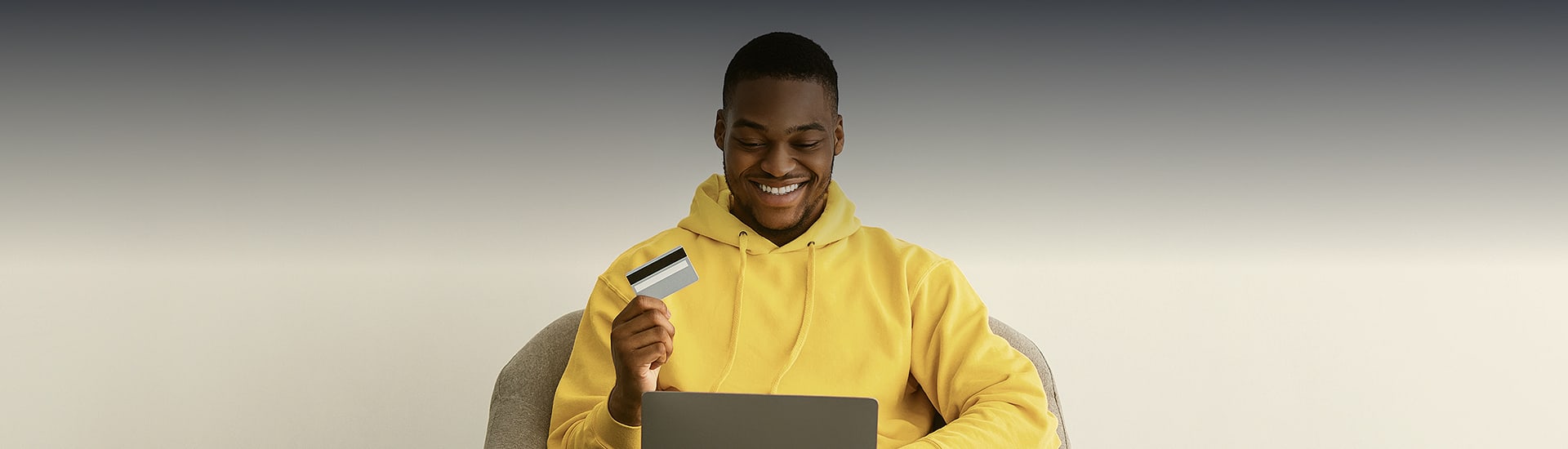 man wearing yellow sweater holding credit card and laptop